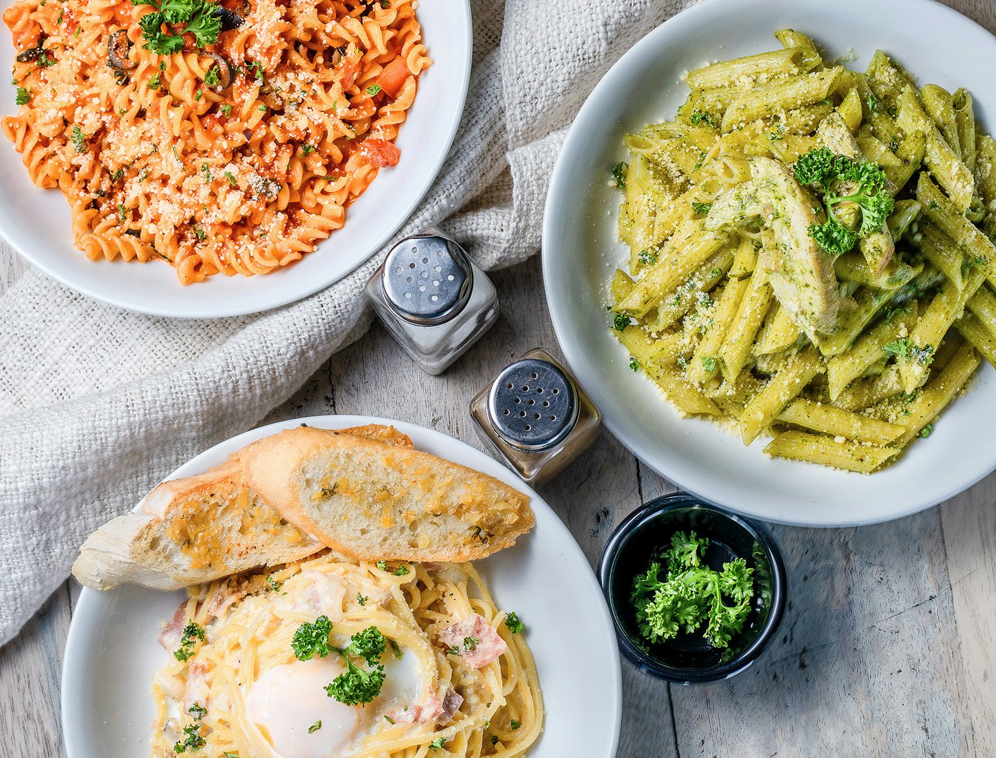 Tre diversi piatti di pasta disposti su un tavolo di legno.