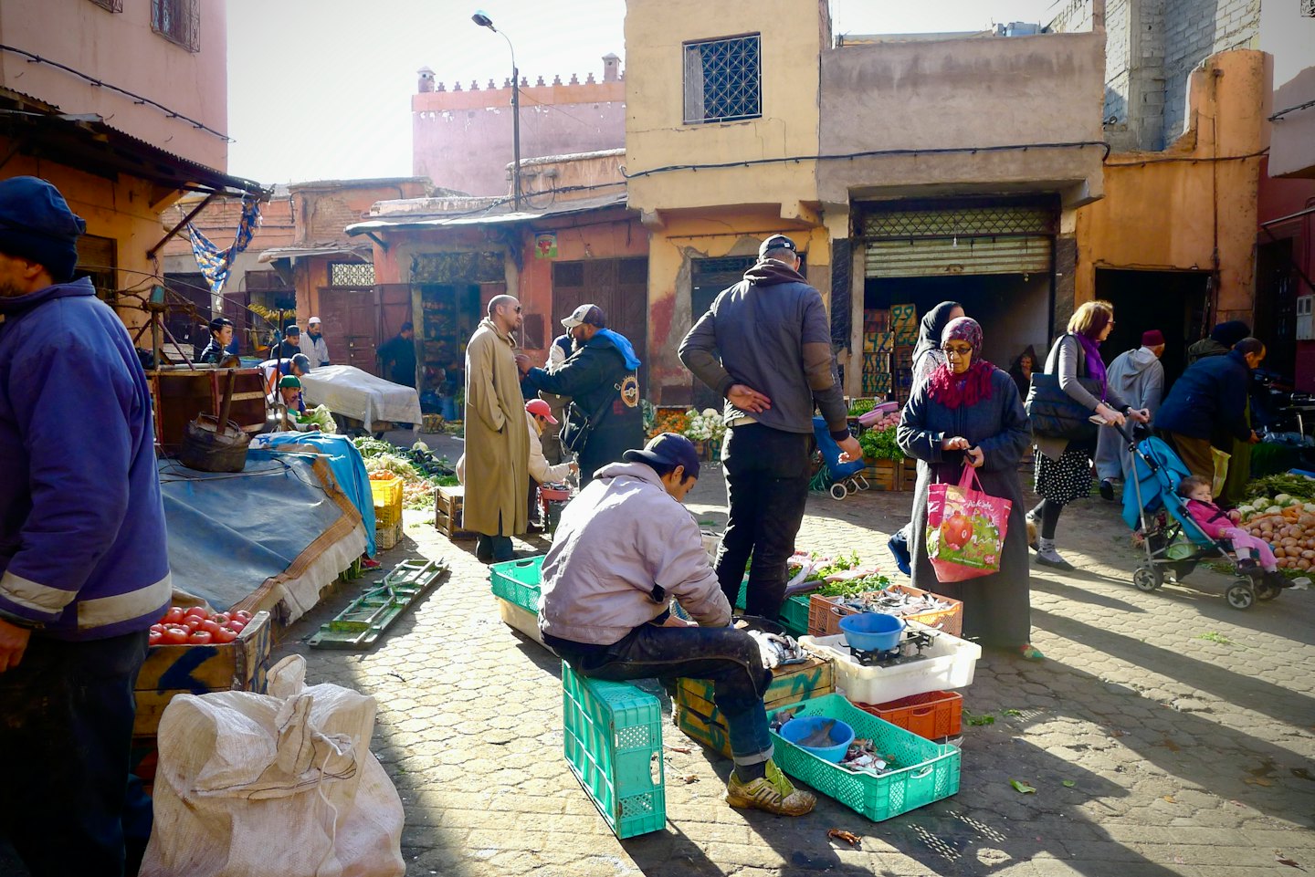 Clienti scelgono frutta e verdura fresca in un vivace mercato all'aperto su strada acciottolata.