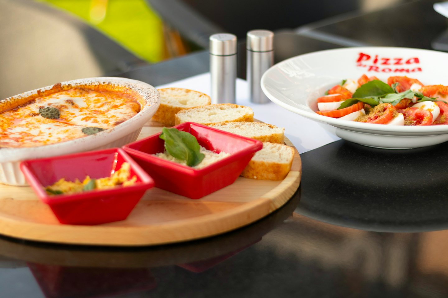 Tavola piena di piatti italiani, tra cui pasta, insalata Caprese e pane.