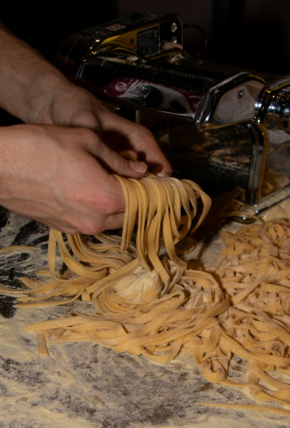 Mani che separano tagliatelle fresche da un mucchio infarinato.